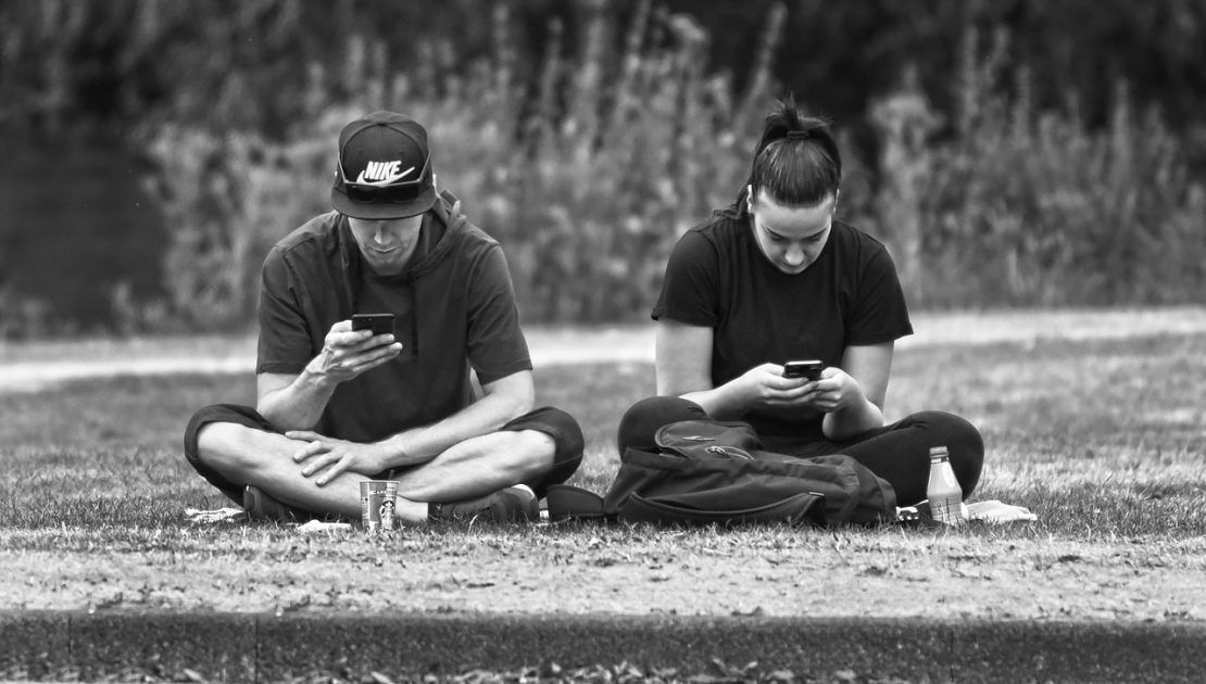 zwei junge Männer mit smartphone sitzen auf einer Wiese